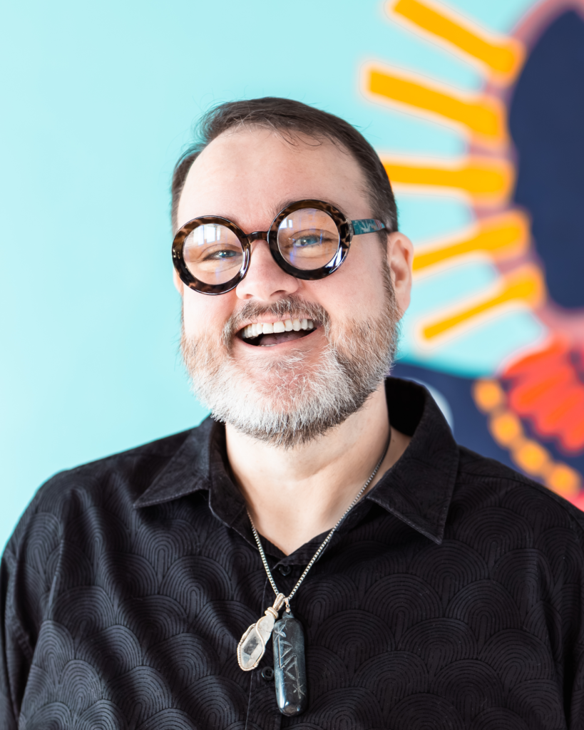 A person laughing with a painting of a sunflower behind them.